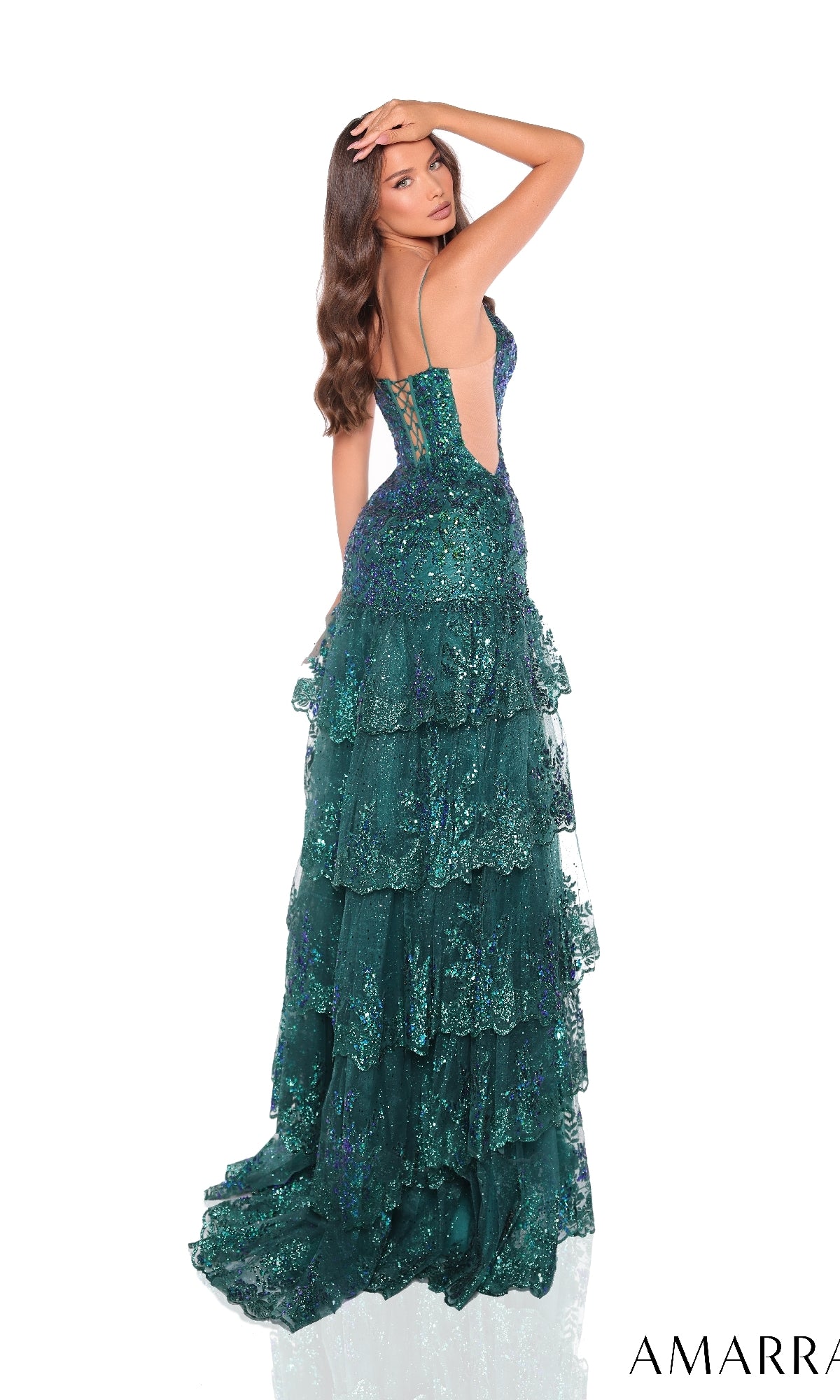 A woman in the Long Formal Dress 88500 by Amarra, a deep green, ruffle-layered gown with thin straps and sequins, poses with one hand on her head, facing away from the camera.